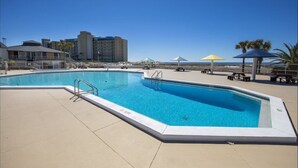 A swimming pool with a clear blue water, surrounded by a paved deck, and a gazebo with a yellow umbrella.