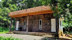 Un bâtiment en pierre avec un toit en bois, deux portes et un petit porche abritant une chaise.