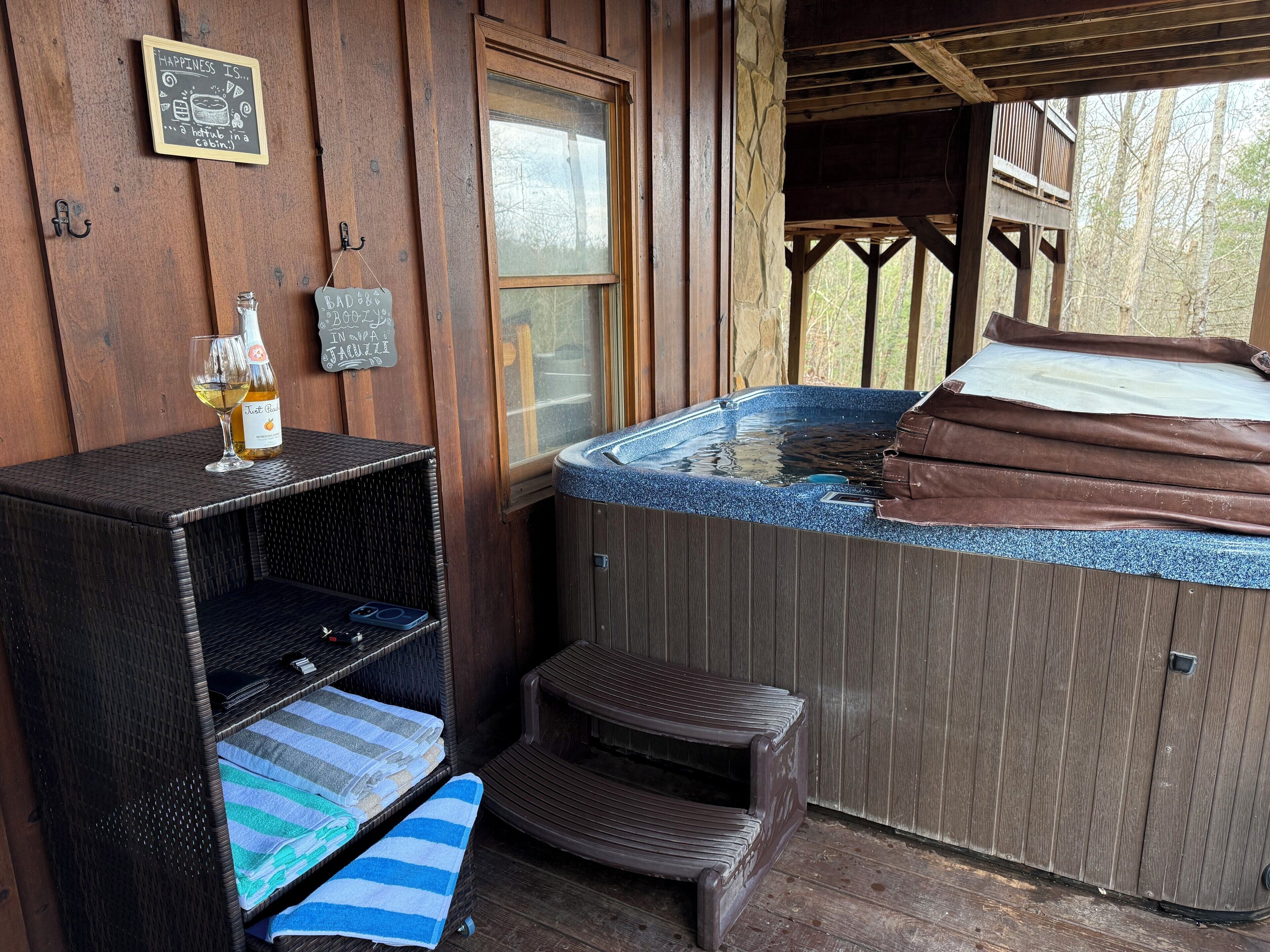 A wooden cabin with a hot tub, a bottle of wine, and towels on a shelf.