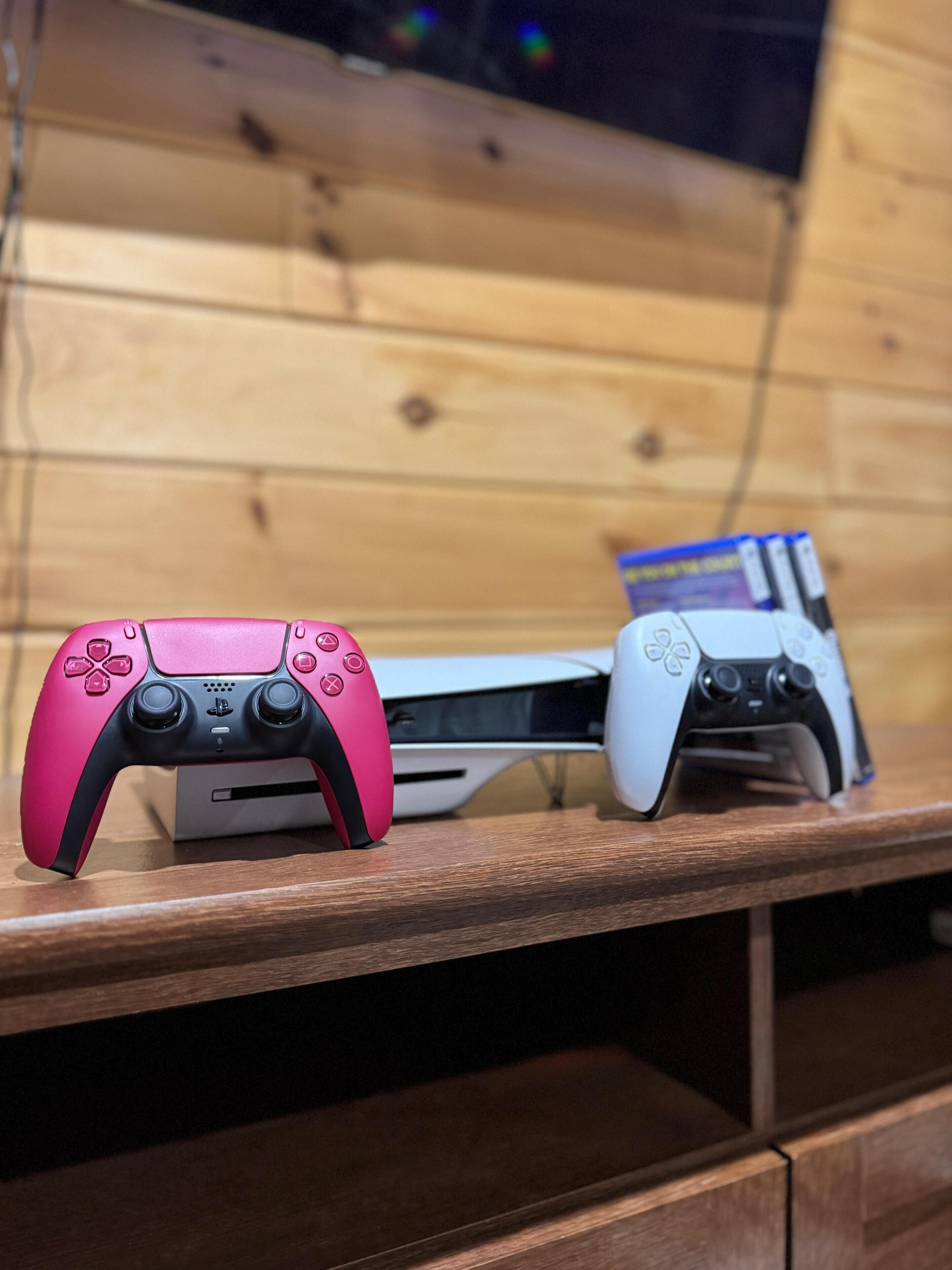A wooden shelf with two gaming consoles and controllers.