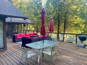 A wooden deck with a glass table and chairs, a red sofa, and a grill. - Dream River Cabin -- Riverfront (blue river)