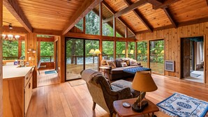 Een houten hut interieur met een eethoek, een bank en een groot raam met uitzicht op een bebost gebied.
