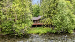 Een chalet omringd door dicht bos, met een heldere beek ervoor.