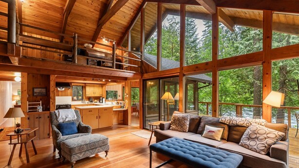Een ruime hut met een grote eethoek, een gezellige woonkamer met een bank en voetenbankje, en een keuken met uitzicht op het bos.