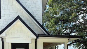 A modern house with a white exterior, a black front door, and a covered porch with a wooden deck. - Luxurious Lakefront retreat with own private dock. (Chapin)