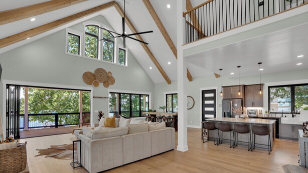 A spacious living area with a large sofa, wooden flooring, and a high ceiling with exposed beams. - Luxurious Lakefront retreat with own private dock. (Chapin)