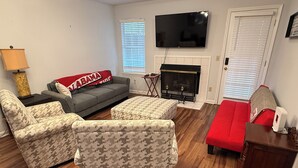 A living room with a sofa, two armchairs, a red couch, a fireplace, and a TV mounted on the wall. - Conveniently Located 2B/2BA Very Close to University of Alabama Campus (Tuscaloosa)