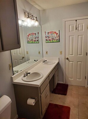 A bathroom with two sinks, a mirror, a toilet, and a door.