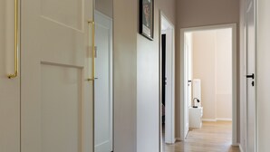 Un pasillo con puertas blancas, un cuadro enmarcado en la pared y un baño visible con inodoro y lavamanos.