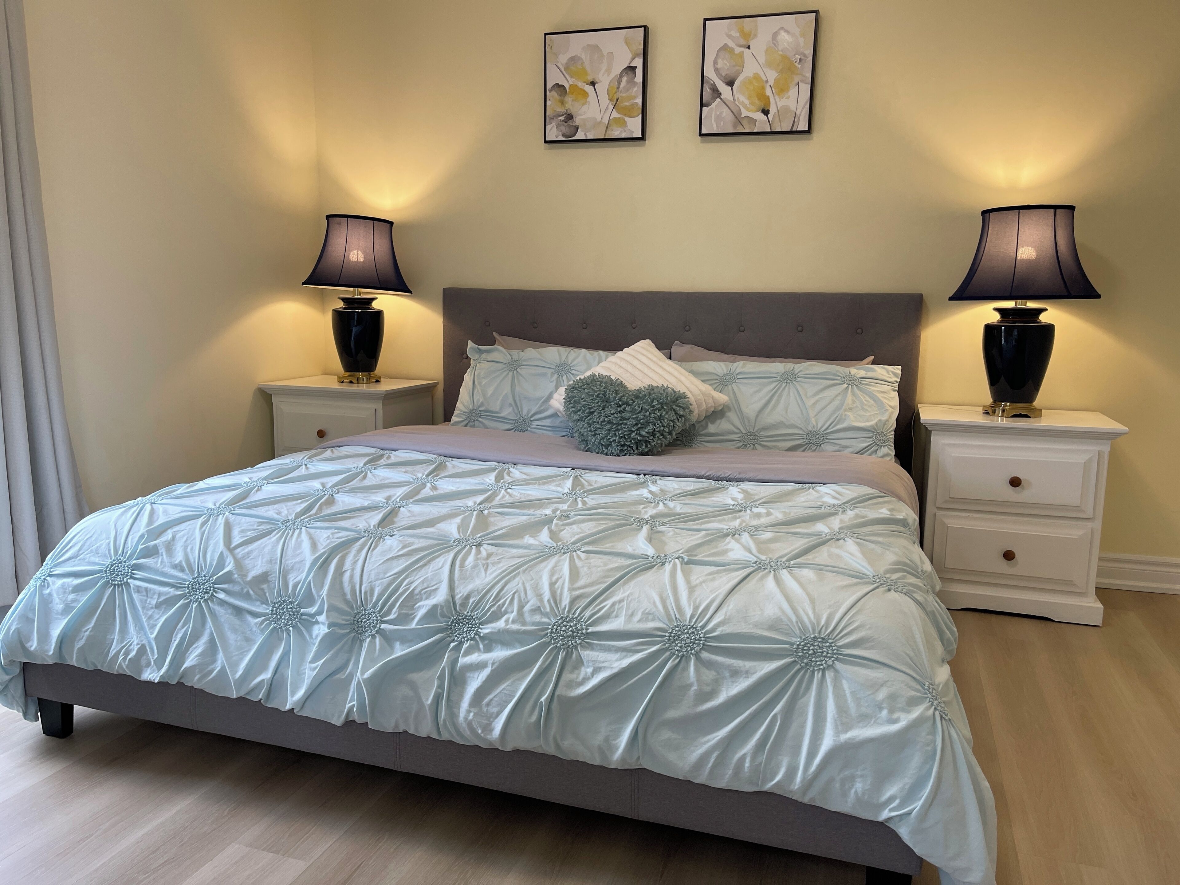 A bedroom with a large bed, two bedside tables, two lamps, and two wall art pieces.