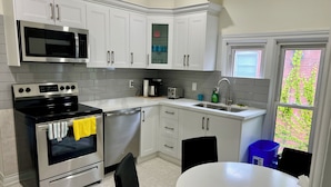 A modern kitchen with white cabinets, stainless steel appliances, a built-in microwave, and a dishwasher. There is a window with a view of greenery outside.