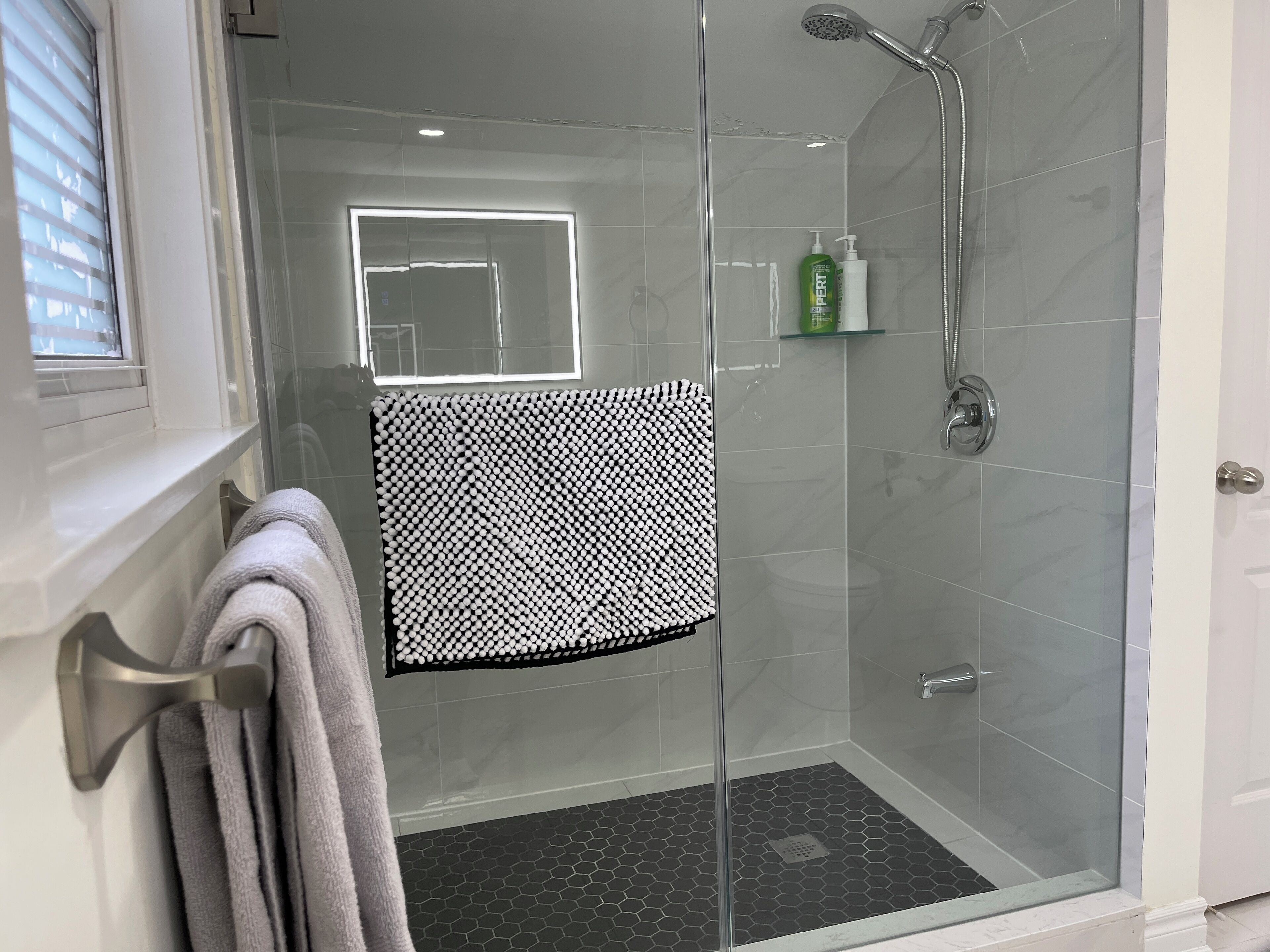 A modern shower area with a glass door, a towel rack with towels, a showerhead, and a small shelf with toiletries.