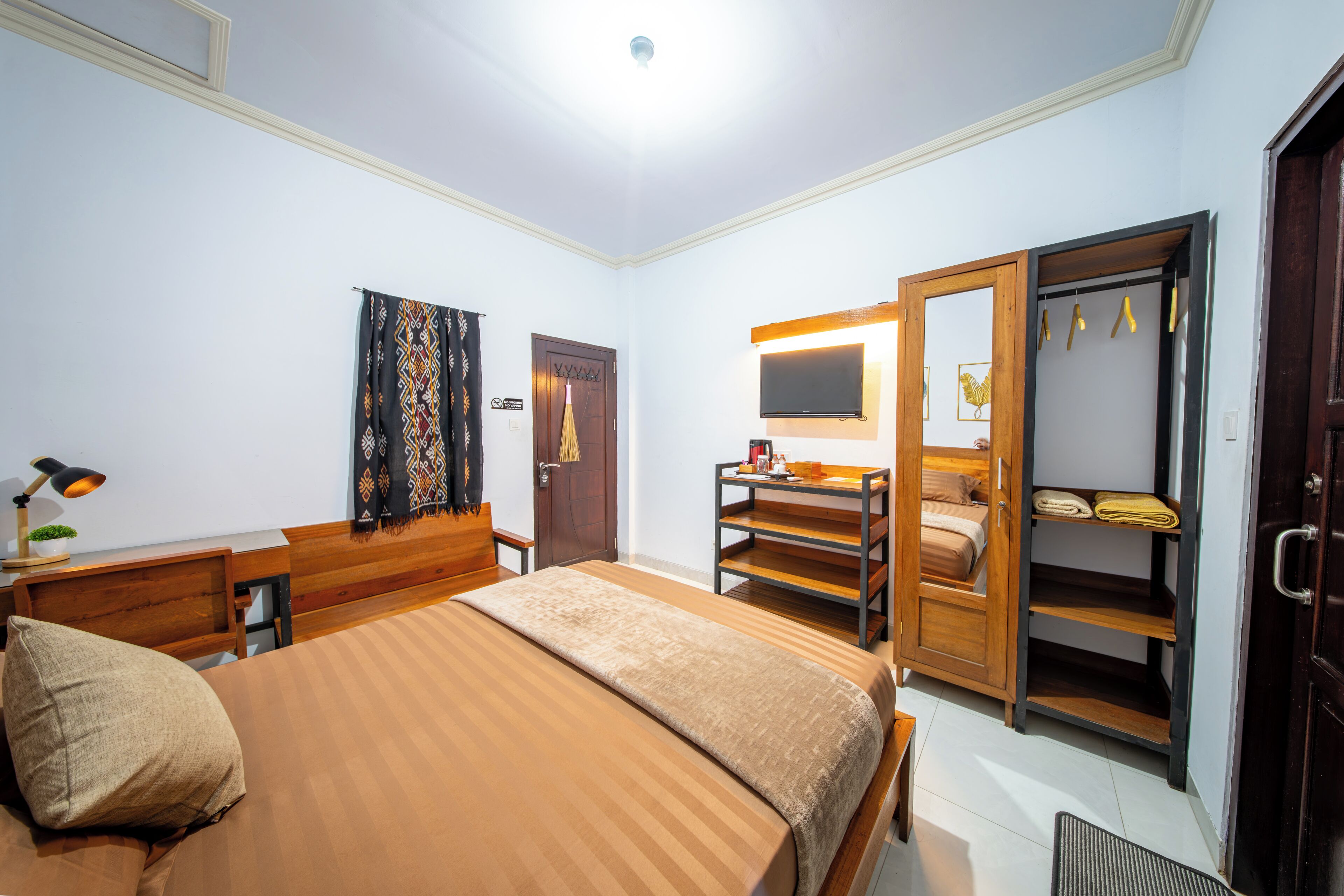 A hotel room with a bed, a desk, a chair, a wardrobe, a mirror, and a television.