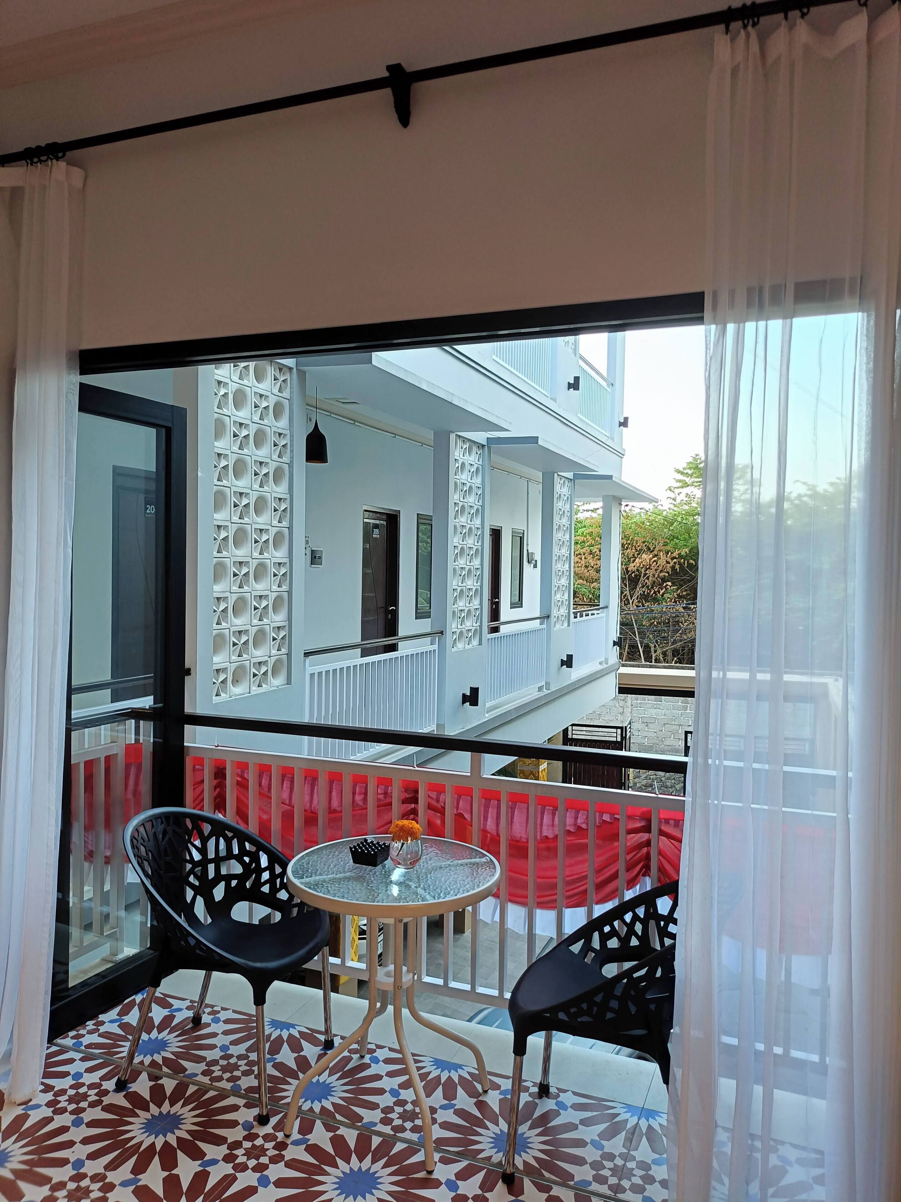 A balcony with two chairs and a small table, a patterned floor, and a view of a white building with balconies.