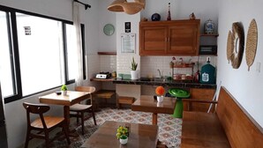 Een kleine keuken met houten kastjes, een eethoek met een tafel en stoelen, en een raam dat voor daglicht zorgt.
