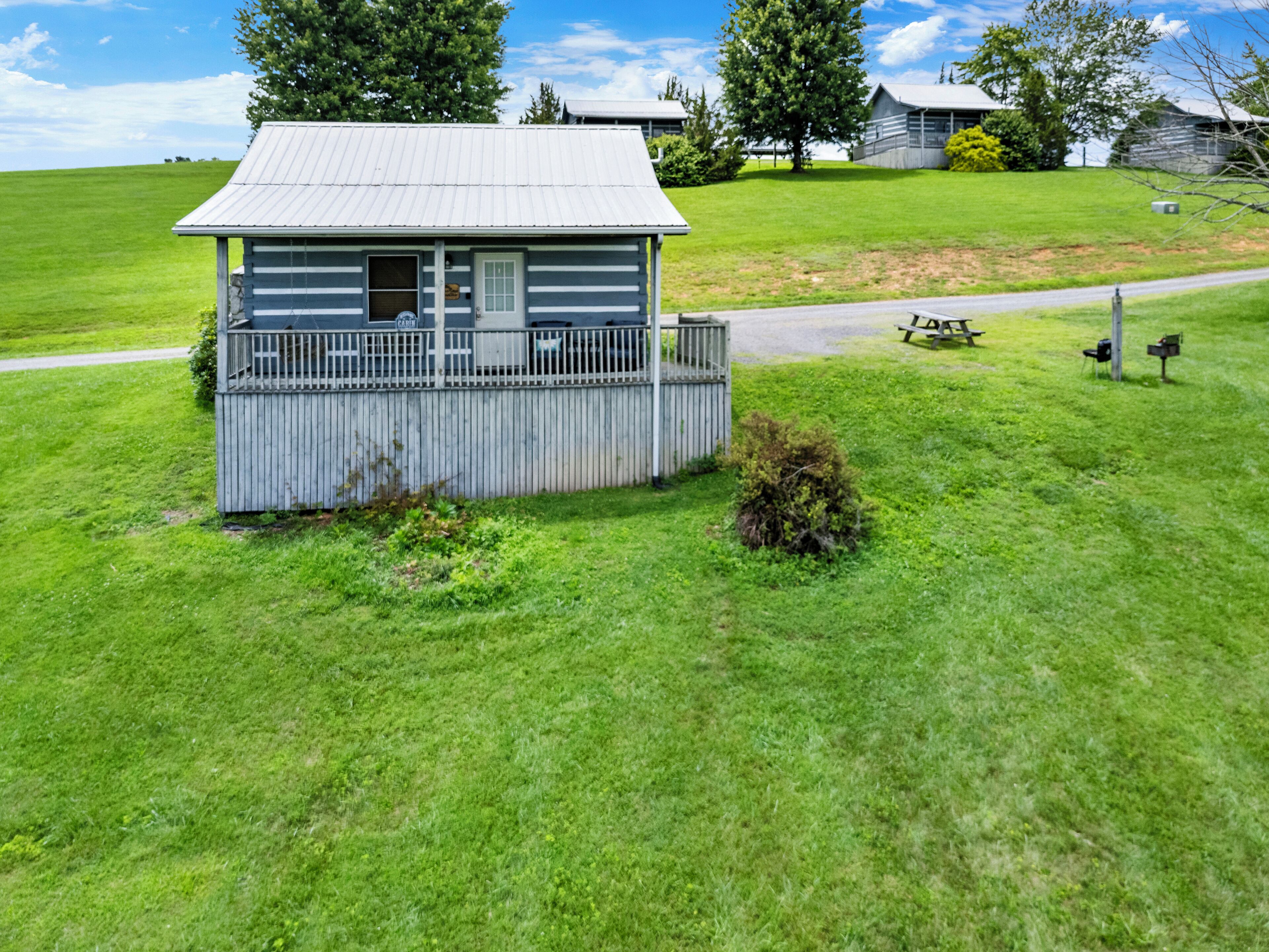 A small cabin with a porch, surrounded by a grassy field and trees.
