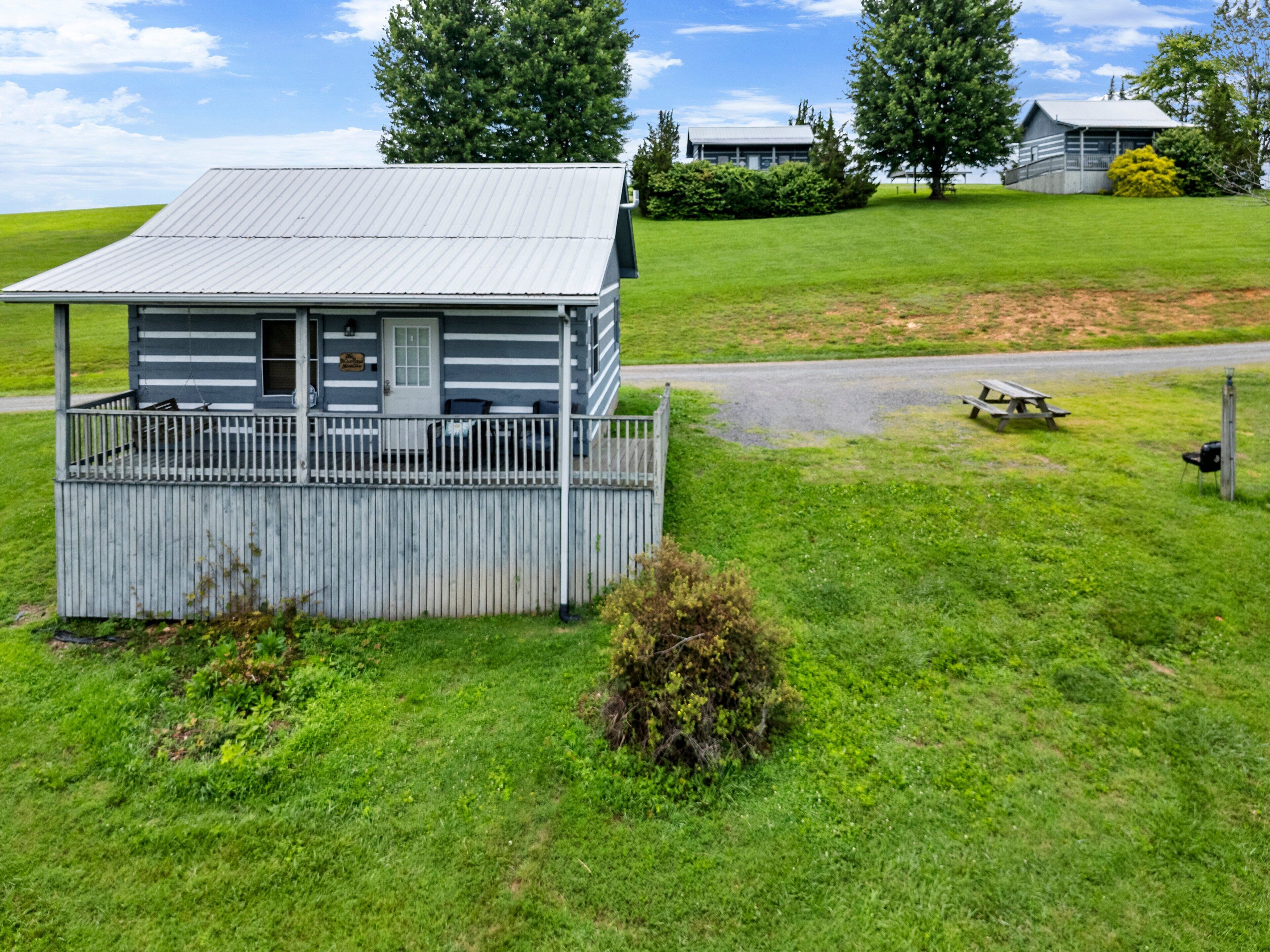Une petite cabane dotée d’un porche et d’une terrasse entourée de clôtures, le tout niché au milieu d’une pelouse verdoyante et d’arbres.