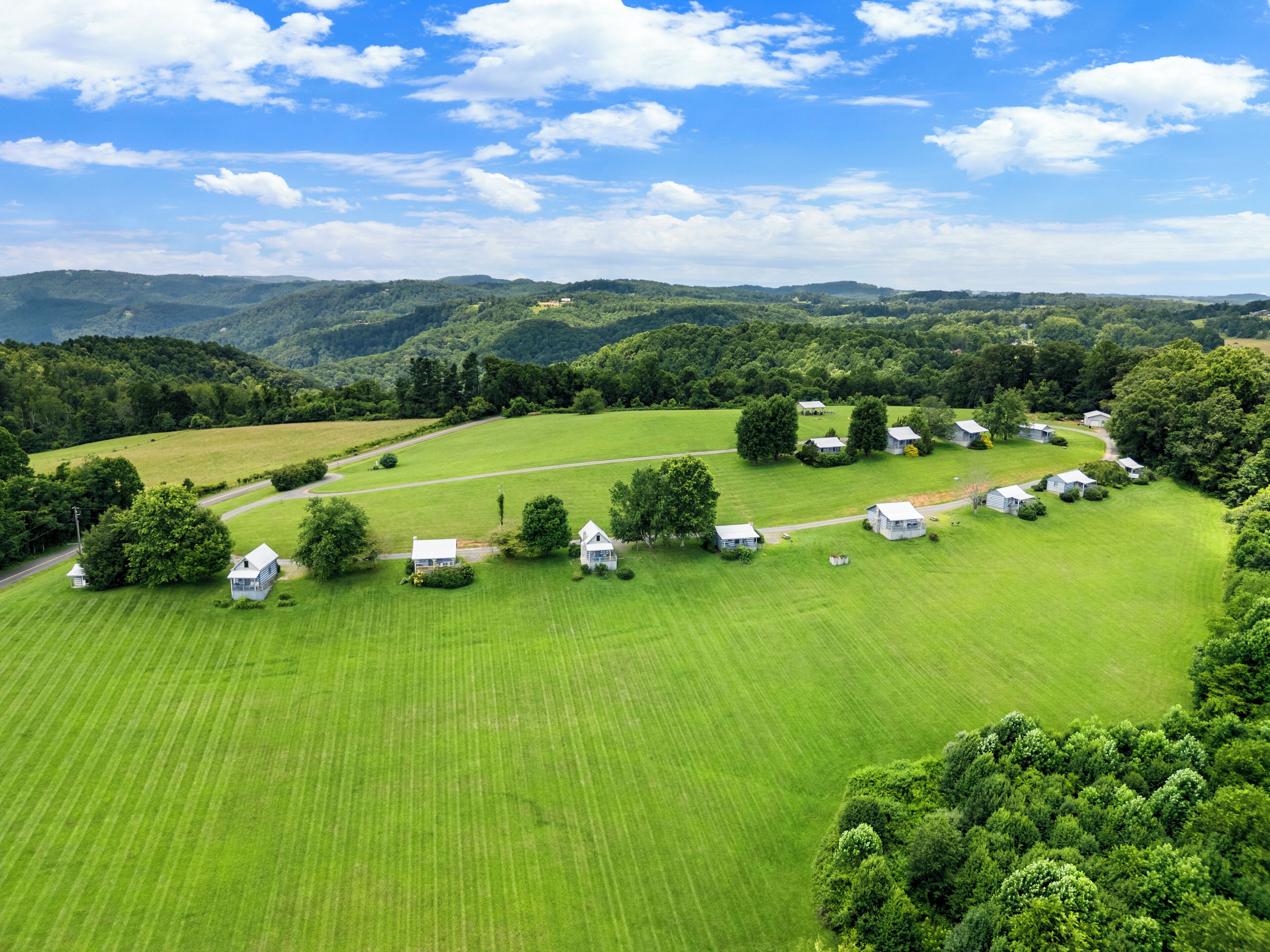 A rural landscape with a series of white houses arranged in a semi-circle, surrounded by lush green fields and trees.