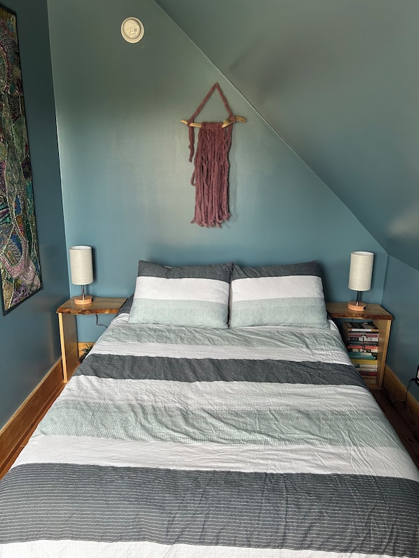 A bedroom with a bed, two bedside tables, a wall-mounted macrame piece, and a bookshelf. - Cozy home in the heart of Advocate Harbour, Pet friendly! (Advocate Harbour)