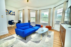 Un salon moderne avec un canapé bleu, une table basse blanche et un coin repas avec des chaises bleues.