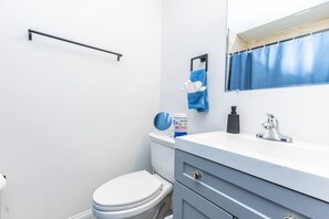 Une salle de bain avec des toilettes blanches, un lavabo avec un miroir, une serviette bleue et un flacon de savon liquide.