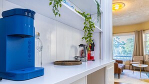 Moderni keittiö, jonka työtasolla on sininen kahvinkeitin, lasipullo ja palosammutin.