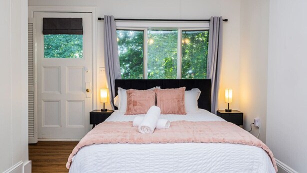 Un dormitorio con cama, dos lámparas de noche, una ventana con cortinas y una puerta.