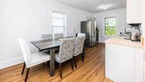 Una cocina compacta con refrigerador, cafetera y comedor con sillas estampadas y una mesa de madera.
