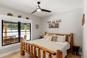 A bedroom with a large bed, a ceiling fan, a window with a view of outdoor furniture, and wall decorations. - Private Nolin Lake Home with FirePit, Ice Maker, Arcade & Electronic Game Table. (Clarkson)