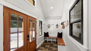 Un pasillo con puerta de madera, un banco y una ventana que da al exterior.