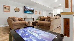 A modern living room with two sofas, a coffee table with a digital display, and a large framed picture on the wall. - Private Nolin Lake Home with FirePit, Ice Maker, Arcade & Electronic Game Table. (Clarkson)