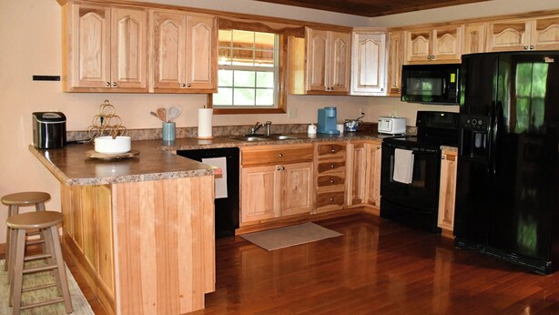 Una cocina con gabinetes de madera, encimera de granito, refrigerador negro, microondas, cafetera y tostadora.