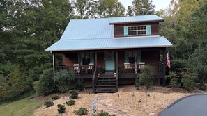A two-story wooden cabin with a porch, a front door, and an American flag.