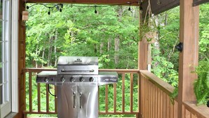 Un espacio al aire libre techado con una parrilla, cubierta de madera y vistas a un bosque.