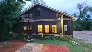 Una casa de madera rústica con un aro de baloncesto, un camino rojo y amarillo, y un patio con césped.