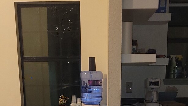 Una cocina con una mesa de madera grande, tres taburetes, un dispensador de agua y un ventanal con vistas.