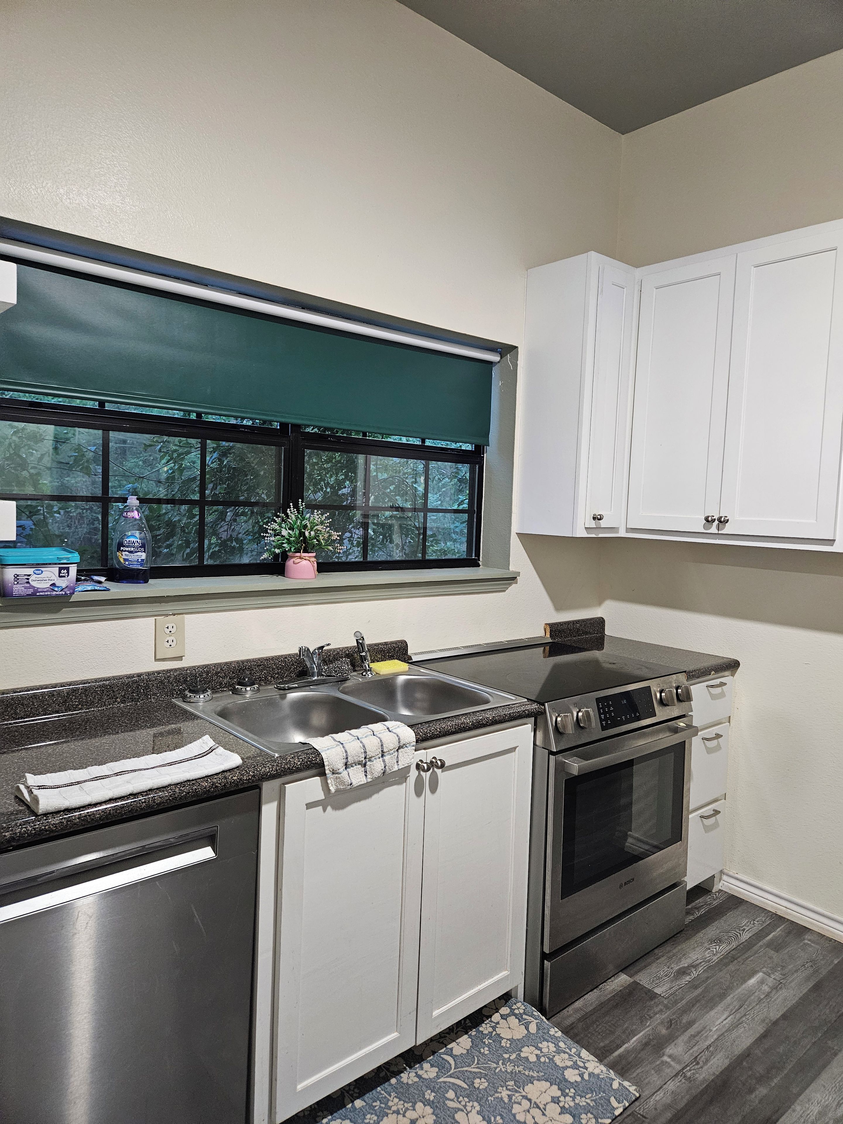 A kitchen with a window, stainless steel appliances, and white cabinets.