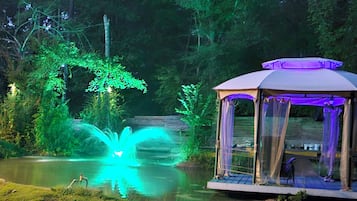A gazebo with a water feature in a forested area.