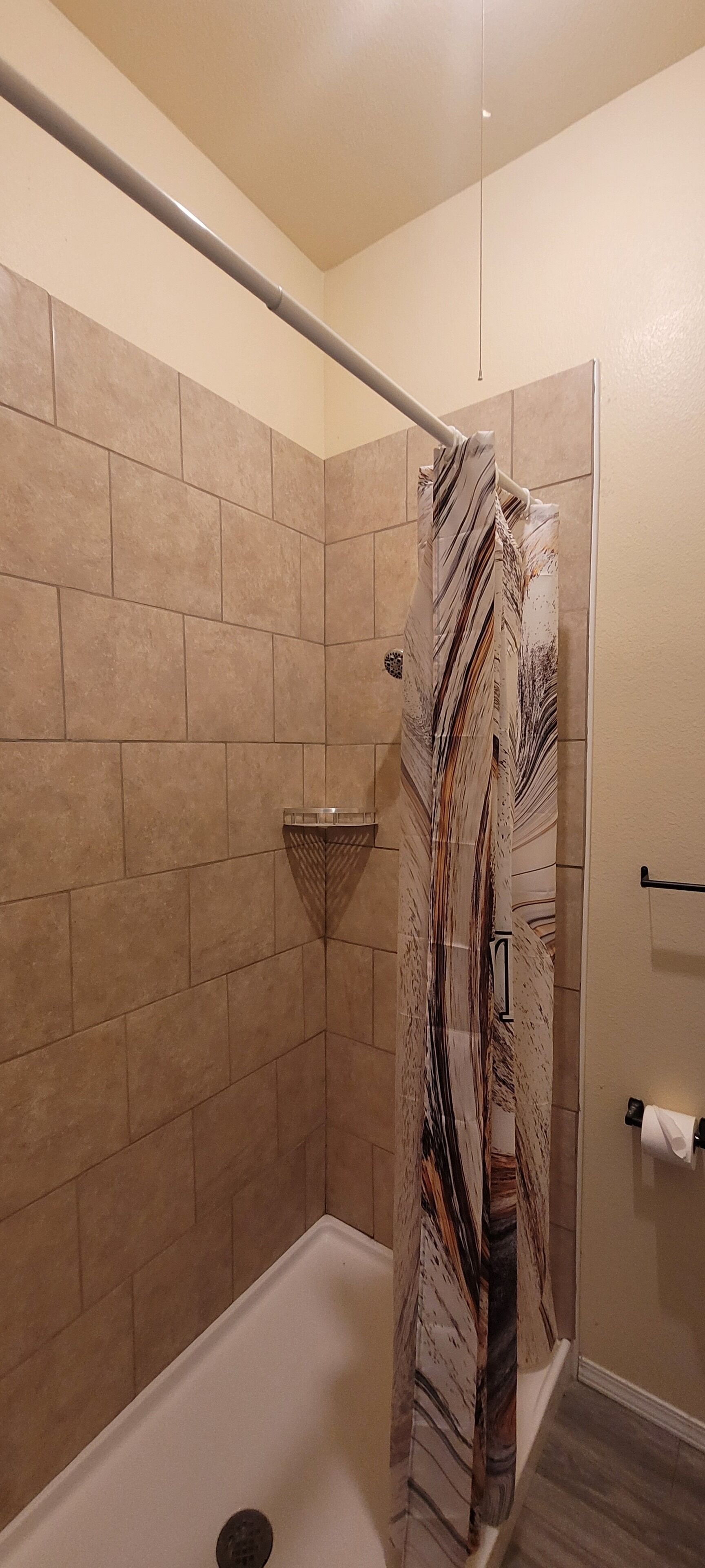 A shower with a marble-patterned curtain, beige tiled walls, and a metal showerhead.