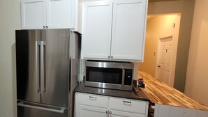 Una cocina con armarios blancos, un refrigerador de acero inoxidable y un microondas Bosch.