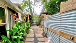 A narrow pathway with a stone-tiled walkway, surrounded by lush green plants and a wooden fence. - Tucked Away Stay in East ATX (Austin)