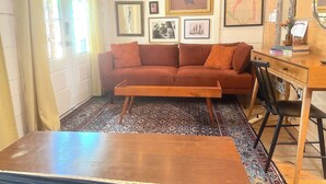 A cozy living room with a sofa, a coffee table, a wooden desk, and a chair. There are framed pictures on the wall and a rug on the floor. - Tucked Away Stay in East ATX (Austin)
