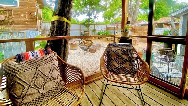A wooden deck with wicker chairs and a table, surrounded by a wooden fence and trees. - Tucked Away Stay in East ATX (Austin)