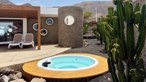 Een modern zwembadgedeelte buiten, met een jacuzzi, omgeven door cactussen en een woestijnlandschap.