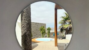Een overzicht van een zwembadgedeelte met een stenen muur, een houten pergola en een palmboom.