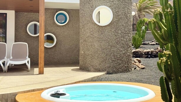 Een zwembadgedeelte met een jacuzzi, omringd door stoelen en een stenen pilaar met ronde uitsparingen.