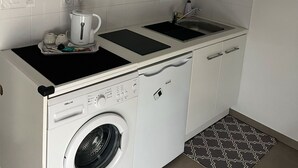 A compact kitchen with a built-in washer and dryer, a coffee maker, and a hanging sign with French phrases. - Studio Near LDLC ARENA OL (Décines-Charpieu)