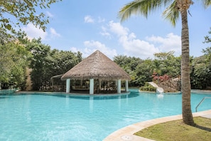 Una piscina cristallina con un gazebo dal tetto di paglia e palme.