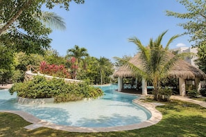 Un'area piscina con una struttura a tetto di paglia, circondata da vegetazione lussureggiante e palme.