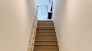 Un escalier en bois avec une rampe, menant à une pièce dont le mur est blanc et qui possède une porte.